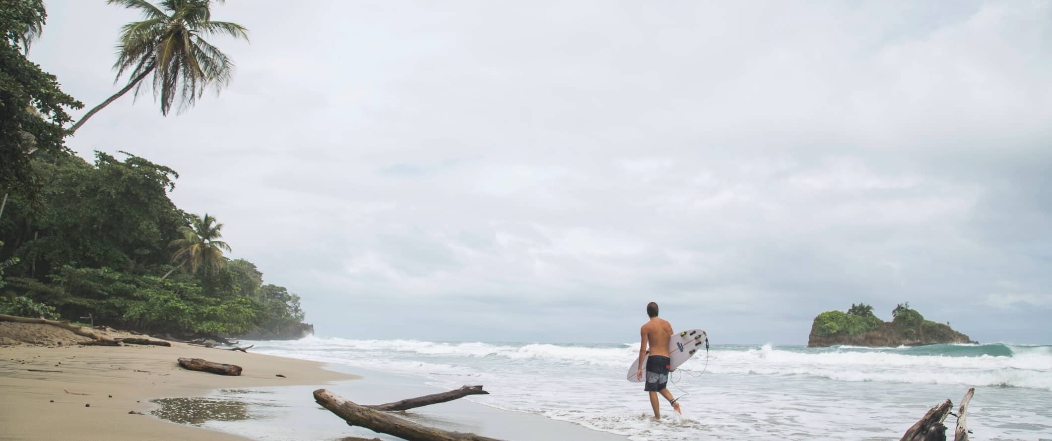Um homem caminha pela praia com uma prancha de surf em Puerto Viejo, Costa Rica