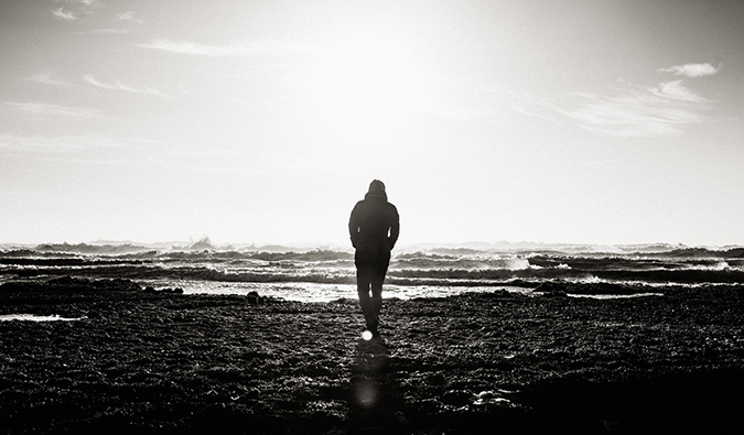 Fotografia em preto e branco de um homem andando sozinho na praia