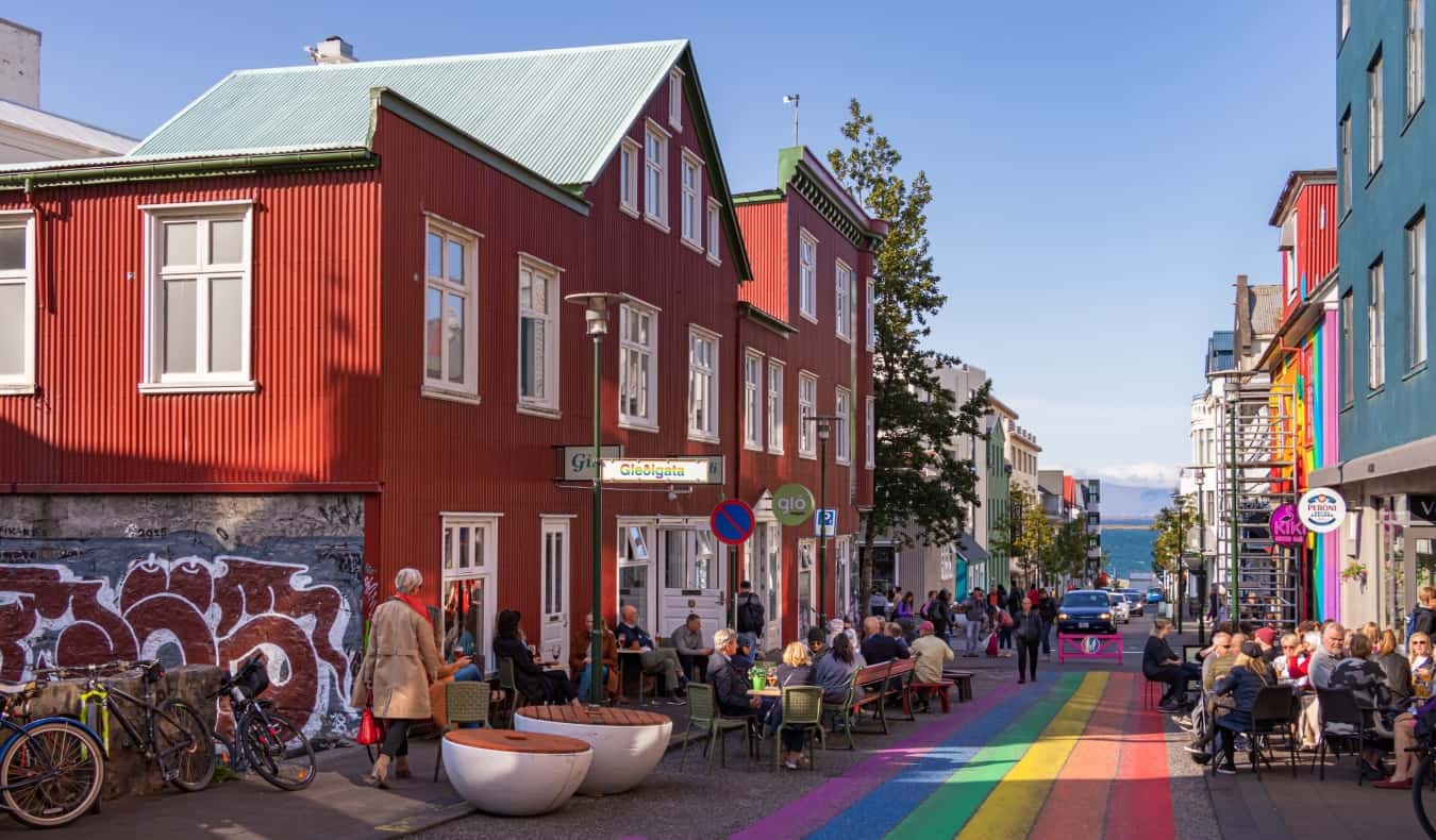 Paisagem de rua em Reykjavik, Islândia, com pessoas sentadas em um café ao longo da rua pintadas em cores do arc o-íris