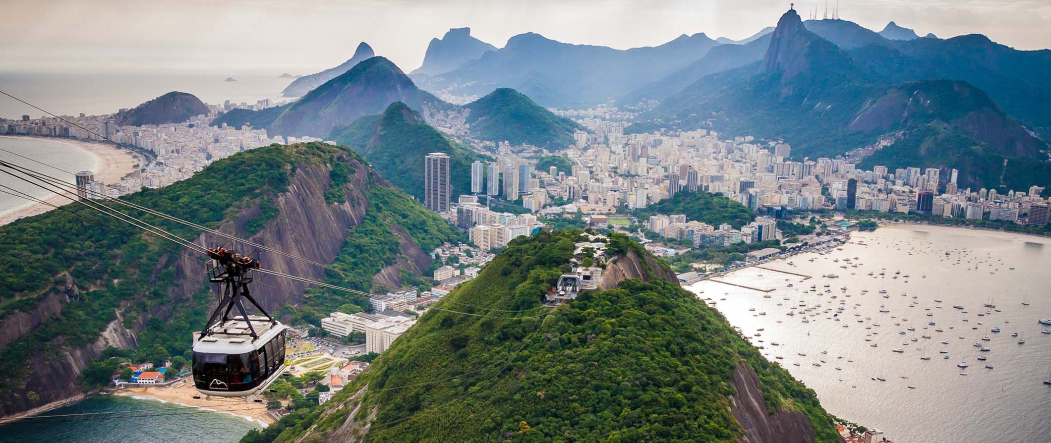 Vista do Rio de Janeiro do Pão de Açúcar com montanhas verdes ao fundo e um teleférico em primeiro plano