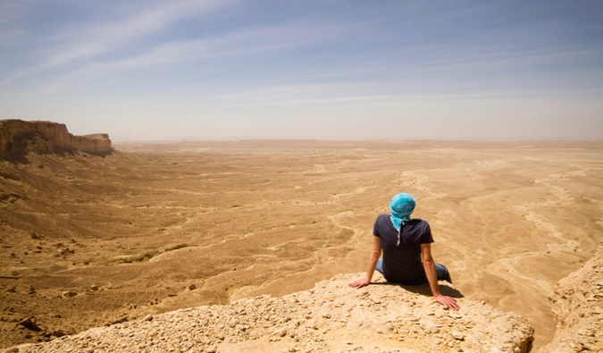 Um único viajante fica em uma pedra em um deserto na Arábia Saudita