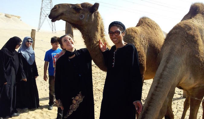 Uma mulher ensinando numa fazenda de camelos na Arábia Saudita, vestida com roupas do Oriente Médio.