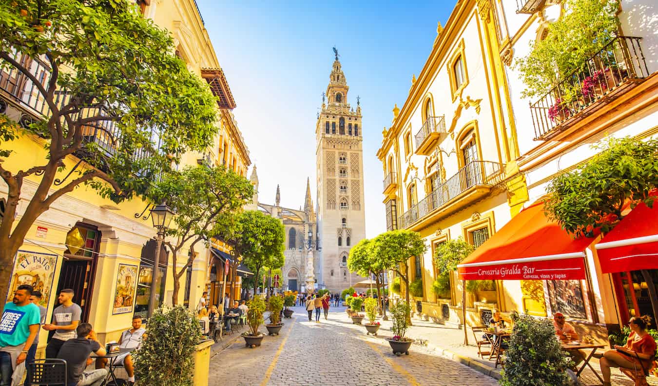 As pessoas andam ao longo de uma rua estreita tranquila em Sevilha, Espanha, Espanha, com uma torre da igreja à distância