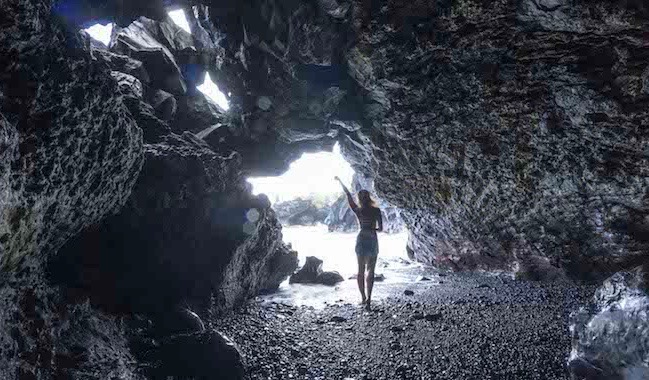 Um viajante solitário posa para uma foto em uma caverna perto do oceano.