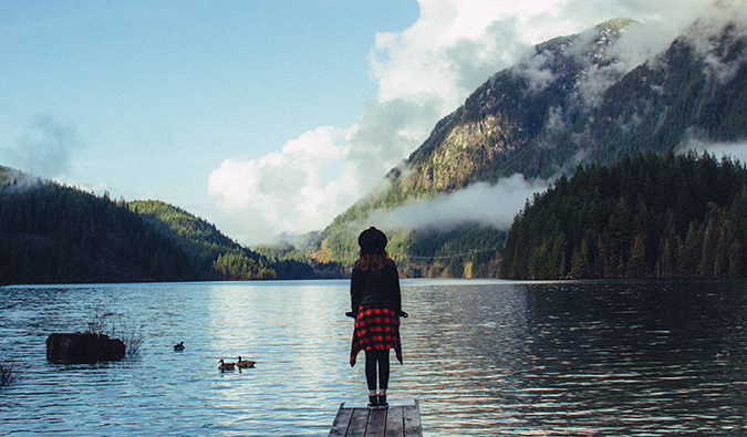 Uma mulher de pé no píer com vista para o lago alpino