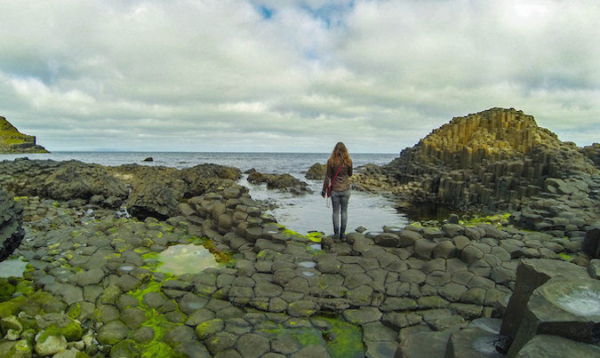 Solitária-mulher-viajante olha para a bela paisagem rochosa islandesa pelo oceano