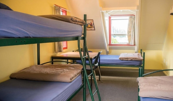 Beliches simples de metal em um quarto amarelo ensolarado no Southern Laughter Backpackers Hostel em Queenstown, Nova Zelândia