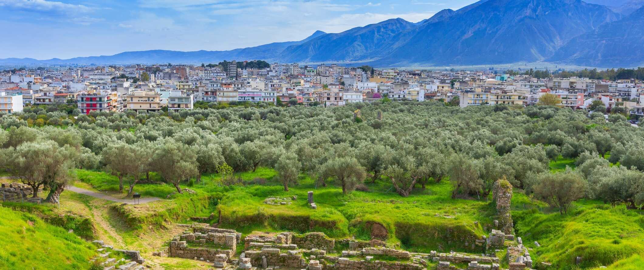 As antigas ruínas em primeiro plano com a cidade moderna de Esparta e as montanhas em segundo plano na Grécia