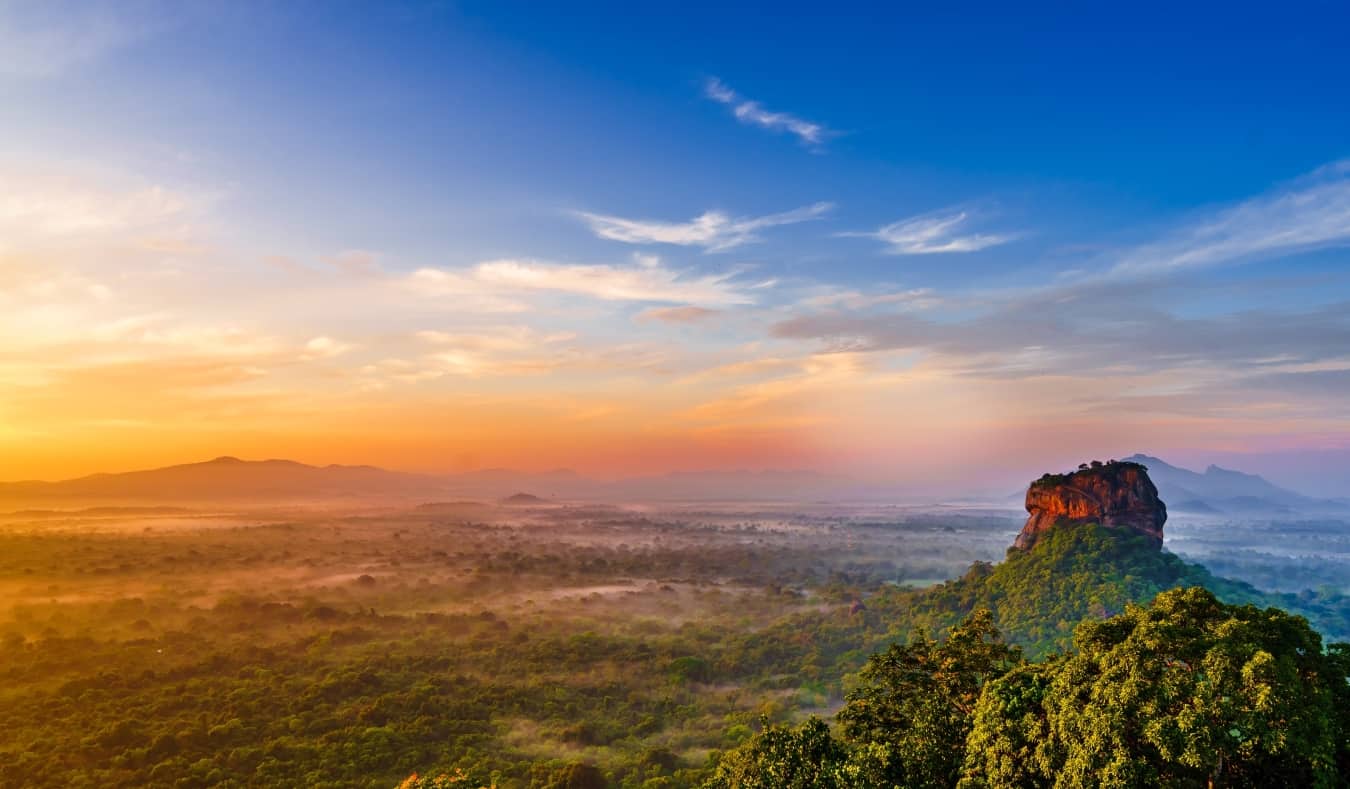 Nascer do sol sobre uma vasta paisagem exuberante com Sigiriya Rock, uma grande formação rochosa que se eleva acima das árvores no Sri Lanka