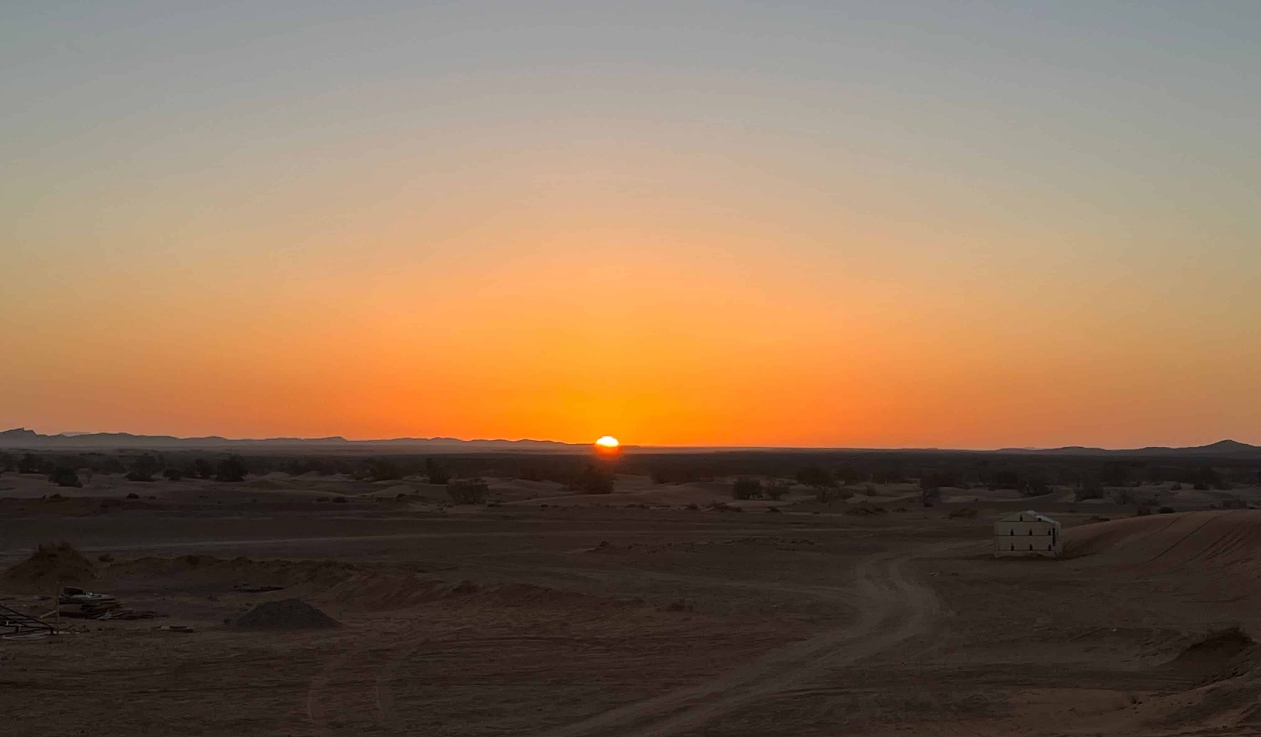 Dunas de areia vermelha cobrindo o horizonte no deserto marroquino ao pôr do sol