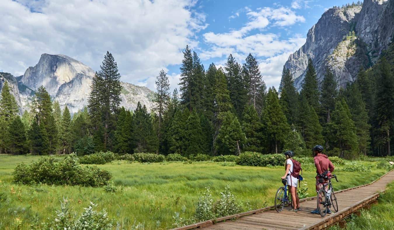 Duas pessoas de bicicleta param e admiram a paisagem de florestas e montanhas no Parque Yosemite, nos EUA.