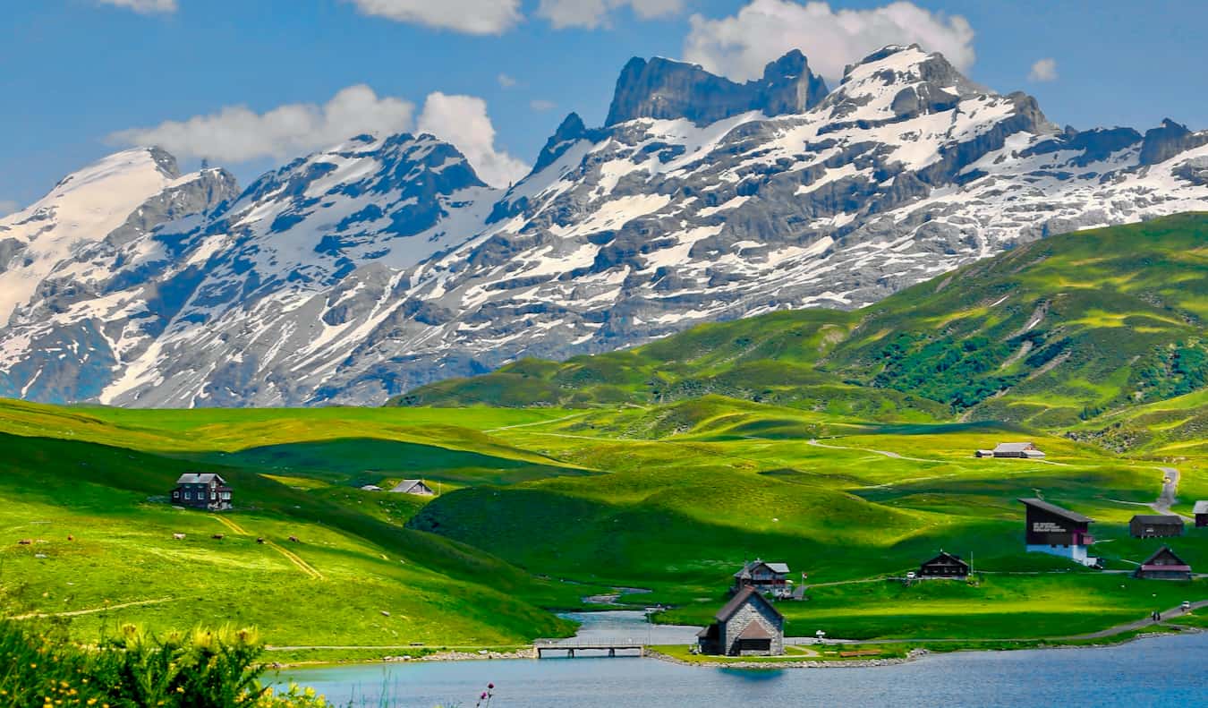 A pitoresca área rural na Suíça, com pequenas casas em uma magnífica colina verde perto da montanha da neve.