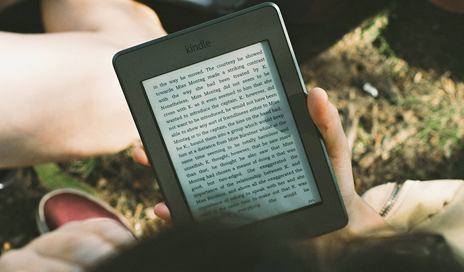O viajante fica na grama e lê em um leitor eletrônico Kindle