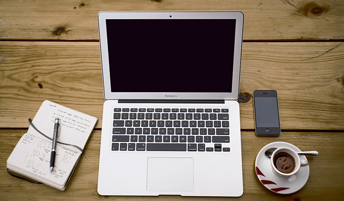Um laptop em uma mesa de madeira com um caderno e uma xícara de café
