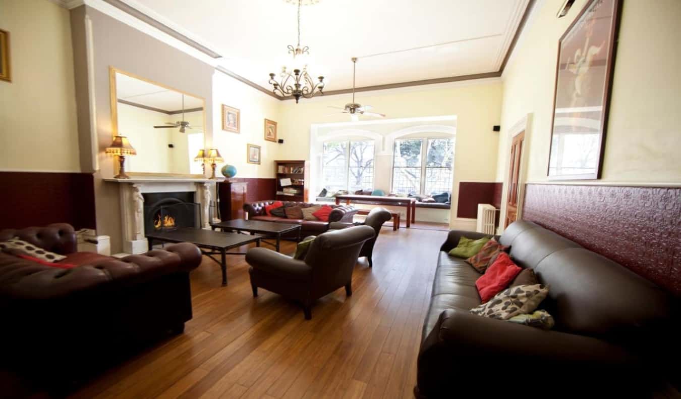Aconchegante, com luz, uma zona comum com muitos sofás, mesas e uma lareira no albergue The Furnery em Melbourne, Austrália.