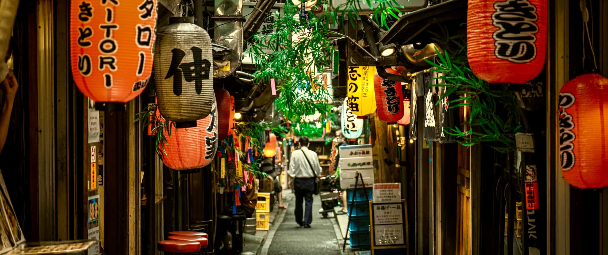 Um homem caminha por um beco estreito repleto de lojas em Tóquio, Japão.