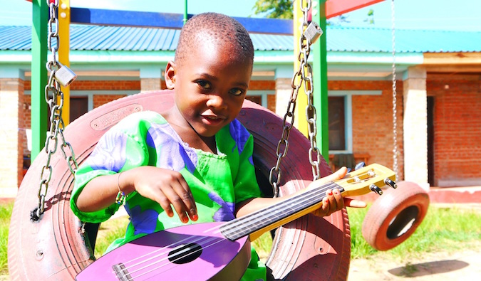 Uma pequena criança africana em roupas coloridas toca uma guitarra pequena
