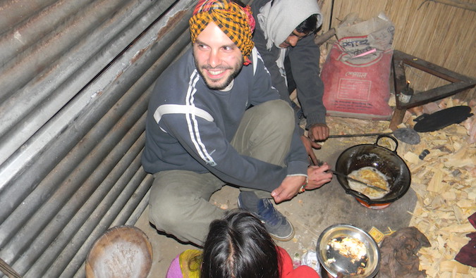 Um único viajante prepara comida em uma pequena cabana com uma família hospedada no exterior