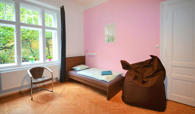 Um quarto com paredes rosa, pufe, cama de casal e grandes janelas no Travel and Joy Hostel em Praga