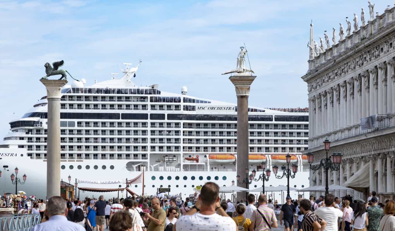 Um navio de cruzeiro tem vista para a histórica Piazza San Marco, em Veneza, Itália. Multidões de turistas são fotografadas em primeiro plano.