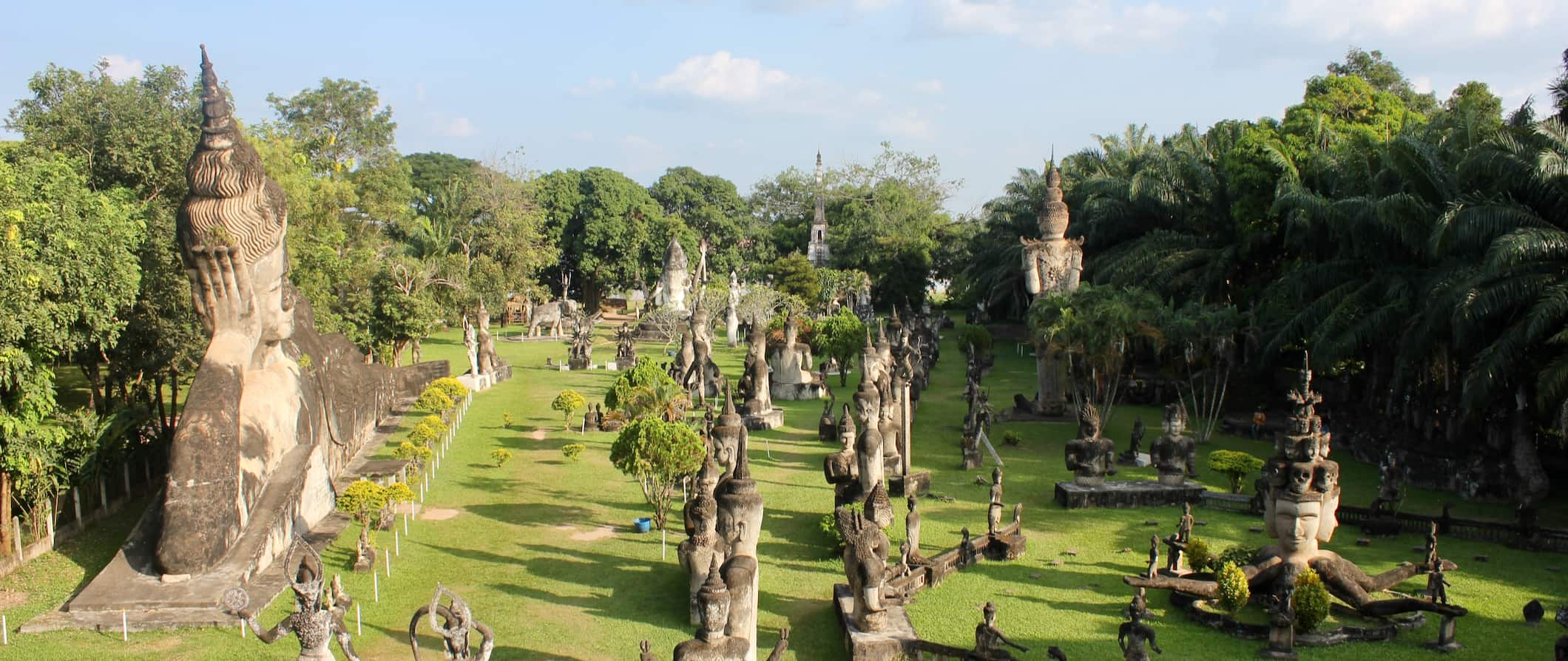 Dezenas de estátuas budistas e hindus no parque de Buda, perto de Vyentnian, Laos, cercado por grama e árvores.