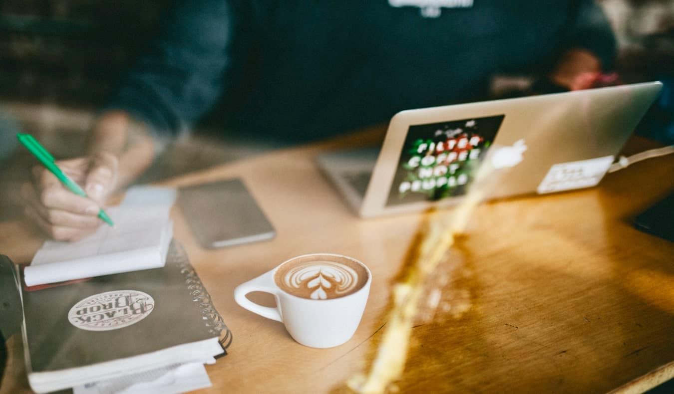 Um homem trabalha na Internet em um café enquanto bebe um café com leite.