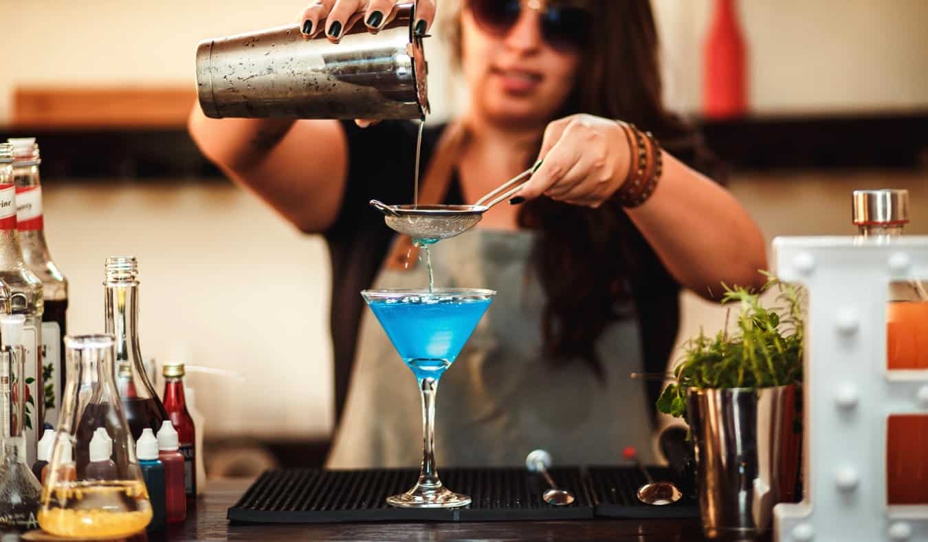 Barman feminina derrama uma bebida colorida no bar
