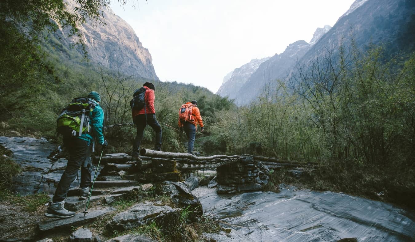 Um grupo de caminhantes atravessa uma ponte de madeira em direção às montanhas da região de Annapurna, no Himalaia.
